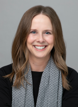 image of a woman with long, light brown hair, blue eyes, and a big smile wearing a black top and a gray patterned scarf.